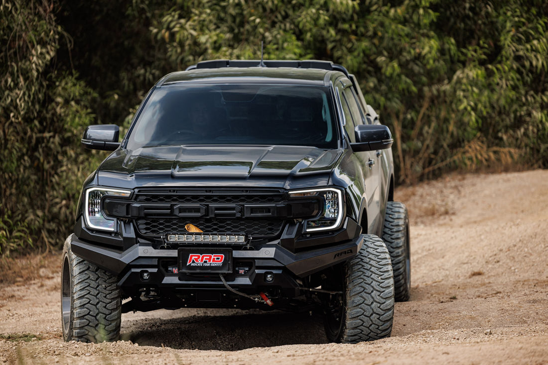 Black Ford pickup driving along a dirt trail through green countryside